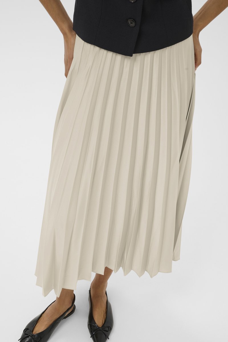 Gonna midi plissettata in beige chiaro, realizzata in un tessuto fluido. Il design presenta pieghe verticali e una forma svasata all'orlo, abbinata a scarpe nere.