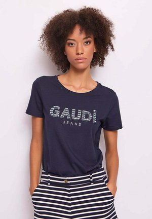 T-shirt in cotone blu navy con logo "GAUDI JEANS" accentuato da cristalli. Abbinato a pantaloni a righe blu navy e bianche, che mostrano uno stile casual.