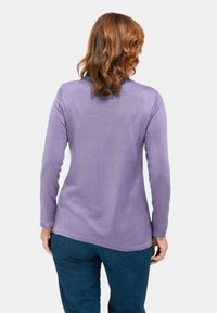 Lavendelfarbenes Langarmshirt aus einem weichen, glatten Stoff. Hat einen abgerundeten Saum, eng anliegende Ärmel und eine dezente, strukturierte Oberfläche.