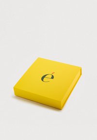 Τετράγωνο κουτί σε ζωηρό κίτρινο με απαλή υφή, με σκοτεινό πράσινο γράμμα «ε» και ένα κόκκινο σημάδι από πάνω.