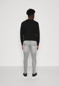 Svart långärmad skjorta, grå slim-fit jeans och svarta sneakers. Slät textur, minimalistisk design och åtsittande silhuett.