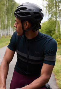 Casque de cyclisme noir avec ouvertures de ventilation, maillot à manches courtes bleu foncé avec des rayures grises, et cuissard de cyclisme bordeaux.