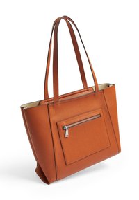 Sac fourre-tout en cuir marron avec deux anses, doté d'une poche zippée à l'avant, présenté sur un fond blanc.