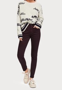 Sweter na kremowym tle z kontrastowym granatowym napisem, ściągacze na rękawach. W zestawie z ciemnofioletowymi rurkami i beżowymi sneakersami.
