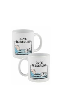 Mug in ceramica bianca con un design che raffigura un personaggio a letto e un cane, insieme al testo "GUTE BESSEERUNG" in grassetto nero.