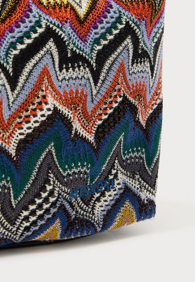Sac en tricot avec un motif en zigzag de couleurs vives, y compris orange, bleu et noir. Surface texturée avec un détail de logo.