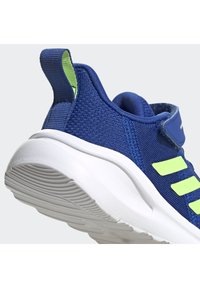 Scarpa sportiva blu con tomaia in rete testurizzata, suola bianca e dettagli verde lime. Presenta un colletto imbottito e un tassello per una facile calzata e svestizione.