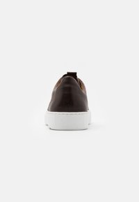 Sneaker in pelle marrone con suola in gomma bianca, caratterizzato da un colletto imbottito, un tassello per il tallone e una superficie liscia, visto da dietro.