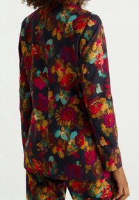 Květinové sako z tmavé látky. Obsahuje výrazné červené, žluté a tyrkysové květiny s hladkou texturou. Dlouhé rukávy a přiléhavý střih.