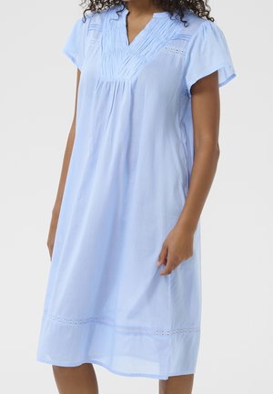 Light blue knee-length dress with short sleeves, v-neckline, and pleated details on the chest, worn by a person with curly hair.
