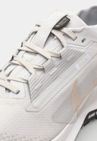 Baskets de course grises claires en textile et matériaux synthétiques. Présentent un motif texturé, des accents réfléchissants et une étiquette GORE-TEX sur la languette.