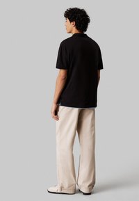 T-shirt nera a manica corta con vestibilità comoda, abbinata a pantaloni beige a gamba larga. L'outfit presenta un look stratificato con orli della camicia visibili.