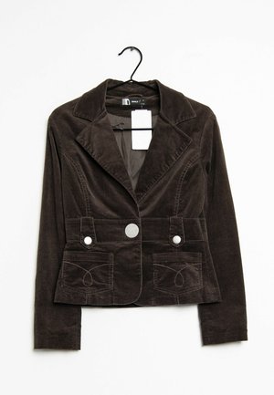 Veste en velours côtelé marron foncé avec un col, deux poches avant et un bouton central, suspendue à un crochet sur un fond blanc.
