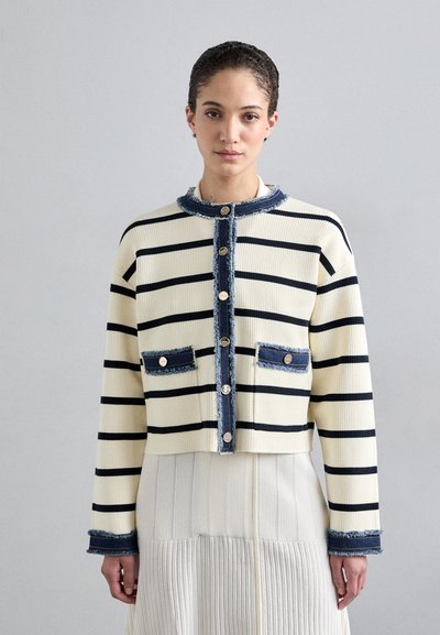 Veste rayée côtelée en crème et marine, avec un design court, des accents en denim, des bords effilochés et des boutons dorés sur le devant et les poches.