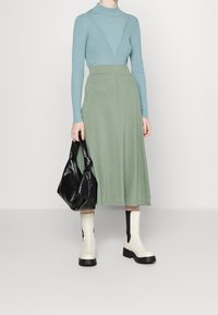 Hellblau gerippter Rollkragenpullover, grüner knielanger Rock, schwarze strukturierte Tasche, cremefarbene Stiefeletten mit schwarzen Akzenten, glatte Texturen.