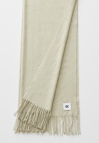Écharpe en laine beige clair avec des franges aux deux extrémités et une petite étiquette blanche portant un logo abstrait noir.