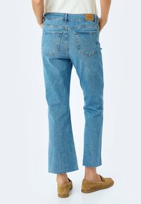 Jeans de mezclilla azul claro con un corte relajado, dobladillos recortados y un desgaste sutil. Presenta bolsillos traseros y una etiqueta de cuero de la marca en la cintura.