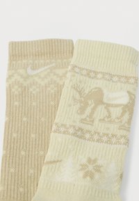 Megzti kojinės smėlio spalvos atspalvių, puošti snaigės ir elnio raštu. Su Nike logotipu. Viršuje yra ribinė tekstūra.