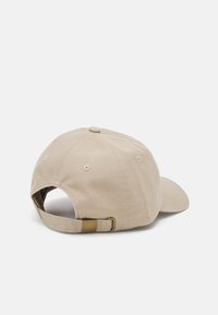 Beige cotton baseball cap with a curved brim, adjustable strap at the back, and a stitched button on top. Minimalist design and texture.
