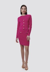 Abito due pezzi fucsia composto da un cardigan cropped con bottoni dorati e una gonna aderente con tasche, entrambi in tessuto testurizzato.