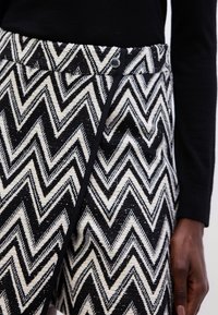 Gonna avvolgente a zig zag in bianco e nero realizzata in tessuto intrecciato, con chiusura a bottone e un contorno a contrasto nero lungo i bordi.