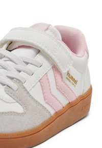 Hvid sneaker med pink detaljer og gråt ruskind. Har en velcrolukning og hvide snørebånd. Guldlogo på siden. Gummisål.