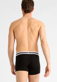 Zwarte boxershorts met een witte gestreepte tailleband, met een nauwsluitende pasvorm en een gladde textuur, ontworpen voor comfort en ondersteuning.