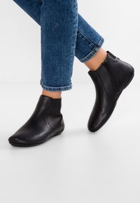Svarta ankelskor i texturerat läder, med en strömlinjeformad design, blixtlås och spetsig tåform. Bärs tillsammans med blå jeans med uppvikta byxben.