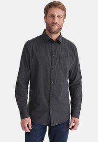 Dunkelgraues Langarmhemd mit einem Button-Down-Kragen, einer Brusttasche und einem karierten Muster. Kombiniert mit dunklen Jeans.
