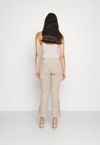 Beige suède flared pants met een gladde textuur en twee achterzakken, gecombineerd met een lichtgrijze tanktop en beige hakken.