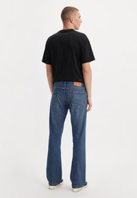 Čierne tričko s krátkym rukávom a modré rozšírené džínsy s červenou značkou na zadnej strane. Denim má klasické umývanie a jemnú štruktúru.