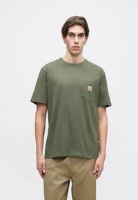 Olivově zelené bavlněné tričko, kulatý výstřih, krátké rukávy, s kapsou na levé straně hrudi a čtvercovým logem. Hladká textura, volný střih.