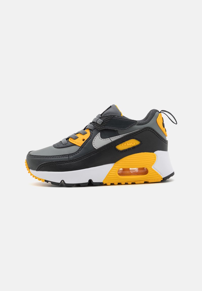 Grå skinn-sneakers med gule detaljer, med en hvit mellomsåle, teksturert sort yttersåle og synlig luftenhet i hælen.