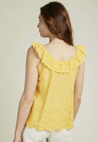 Top sans manches jaune avec un col froncé, ornée de motifs floraux brodés et d'un ourlet en forme de vagues. Tissu léger.