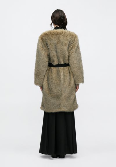 Abrigo de piel sintética en marrón claro con una textura suave, con un cinturón negro en la cintura. Se lleva sobre una falda larga negra, con mangas largas.