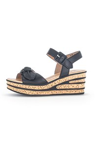 Sandale compensée en cuir noir avec un accent floral surdimensionné à l'avant, bride de cheville réglable et plateforme texturée semblable à du liège.