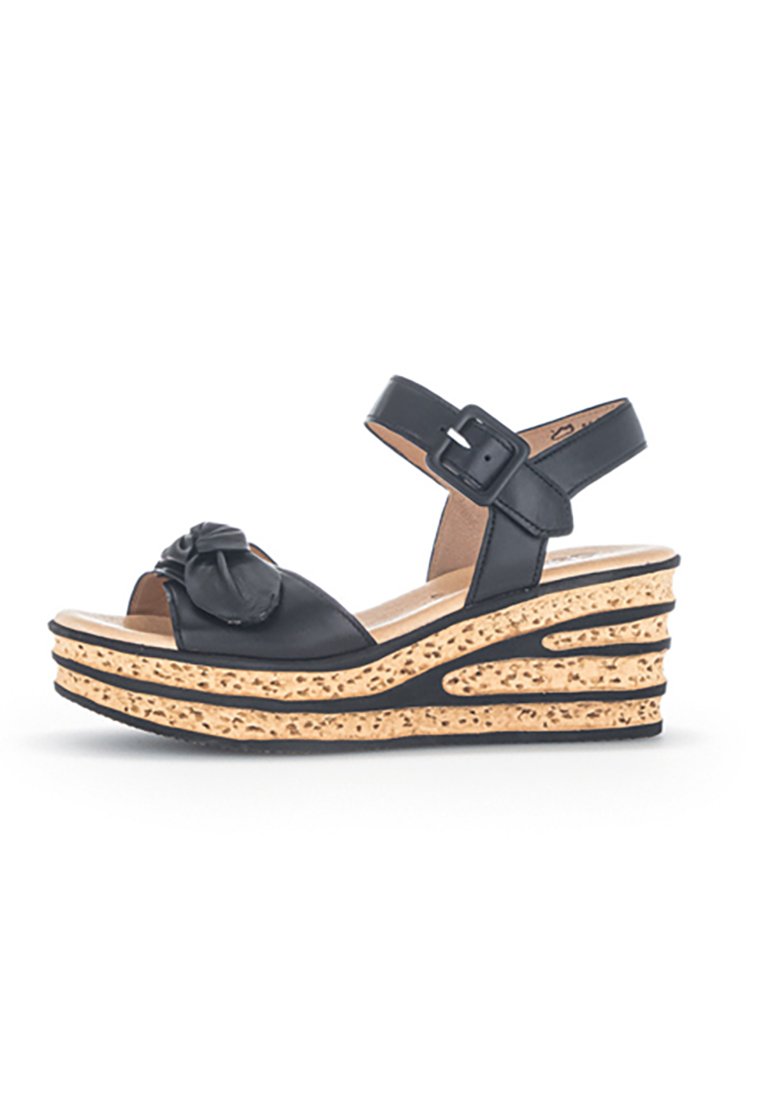 Sandale compensée en cuir noir avec un accent floral surdimensionné à l'avant, bride de cheville réglable et plateforme texturée semblable à du liège.