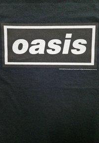 Sort t-shirt med et hvidt rektangulært logo, hvor ordet "oasis" står med fede bogstaver. Blødt, glat tekstur med minimale detaljer.