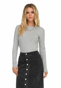 Top grigio chiaro a maniche lunghe con maniche aderenti abbinato a una gonna in denim nera a vita alta con chiusura frontale a bottoni e tasche.