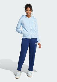 Light blue zip-up hoodie with a front pocket, paired with navy joggers. The outfit features a soft texture and subtle branding on both pieces.