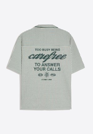 Rövid ujjú, zöld-fehér, függőleges csíkos ing a hátán a „Túl elfoglalt vagyok ahhoz, hogy gondtalan legyek és válaszoljak a hívásaidra” szöveggel.