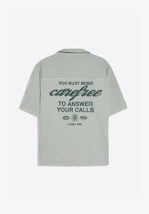 Rövid ujjú, zöld-fehér, függőleges csíkos ing a hátán a „Túl elfoglalt vagyok ahhoz, hogy gondtalan legyek és válaszoljak a hívásaidra” szöveggel.