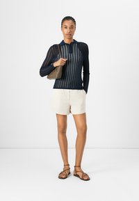 Marineblauwe, langetekst, gebreide top met verticale strepen en een grote kraag, gecombineerd met beige shorts en bruine sandaaltjes met bandjes.