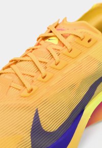 Baskets de course Nike orange vif avec des lacets détaillés et un logo swoosh violet foncé sur le côté, présentées en gros plan anglé.