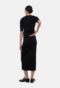 Ensemble noir en maille, composé d'un haut ajusté et d'une jupe mi-longue ornée de petites sequins. Le design comprend des manches courtes et une fente dans le dos.