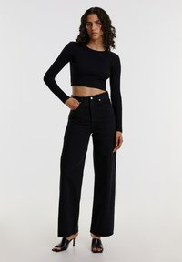 Schwarzes, geripptes, kurzes Langarmoberteil, hoch geschnittene schwarze, weite Jeans und schwarze offene High Heels. Einfaches Design und einfarbige Farben.