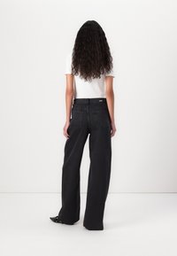 Jeans de mezclilla negros de pierna ancha con cintura alta, costuras visibles y dos bolsillos traseros. Combinados con una camisa blanca de manga corta.