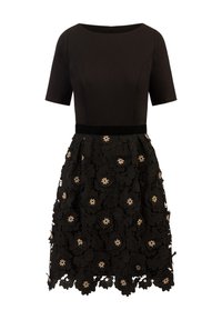 Robe noire avec un corsage ajusté, des manches courtes et une jupe évasée. Jupe ornée de dentelle florale et d'éléments en forme de perles.