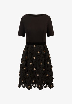 Black dress featuring a fitted bodice, short sleeves, and a flared skirt. Skirt adorned with floral lace and pearl-like embellishments.