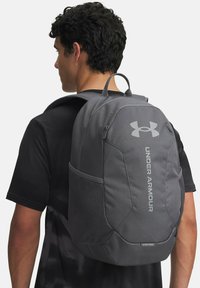 Zaino grigio Under Armour con un design elegante, spallacci regolabili, logo frontale, tasca laterale e una superficie testurizzata per garantire durata.